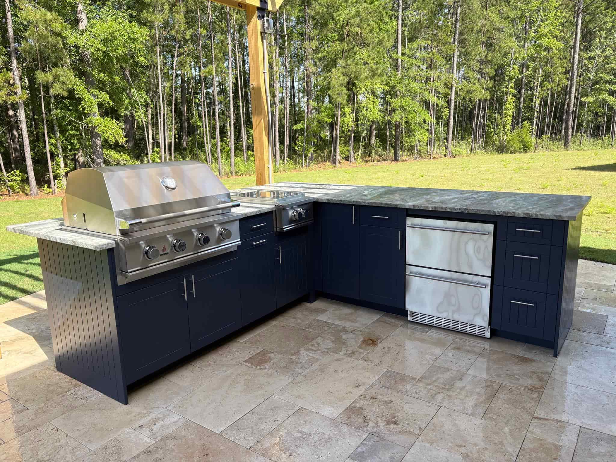 Built-in outdoor kitchen with stone counters and grill beside a Lowcountry pool